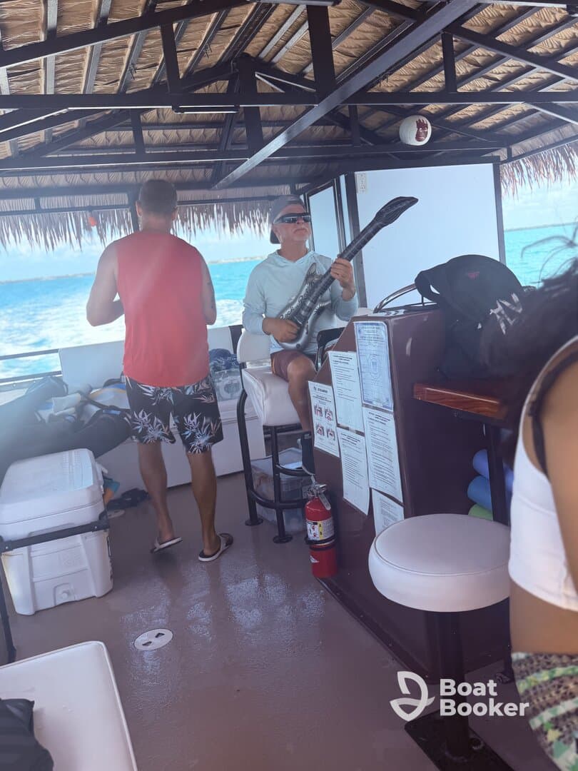Inside view of a boat's cabin featuring guests enjoying the space, with one person playing a guitar-like instrument. This setting showcases the relaxed atmosphere typical of boat outings.