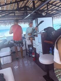 Inside view of a boat's cabin featuring guests enjoying the space, with one person playing a guitar-like instrument. This setting showcases the relaxed atmosphere typical of boat outings.