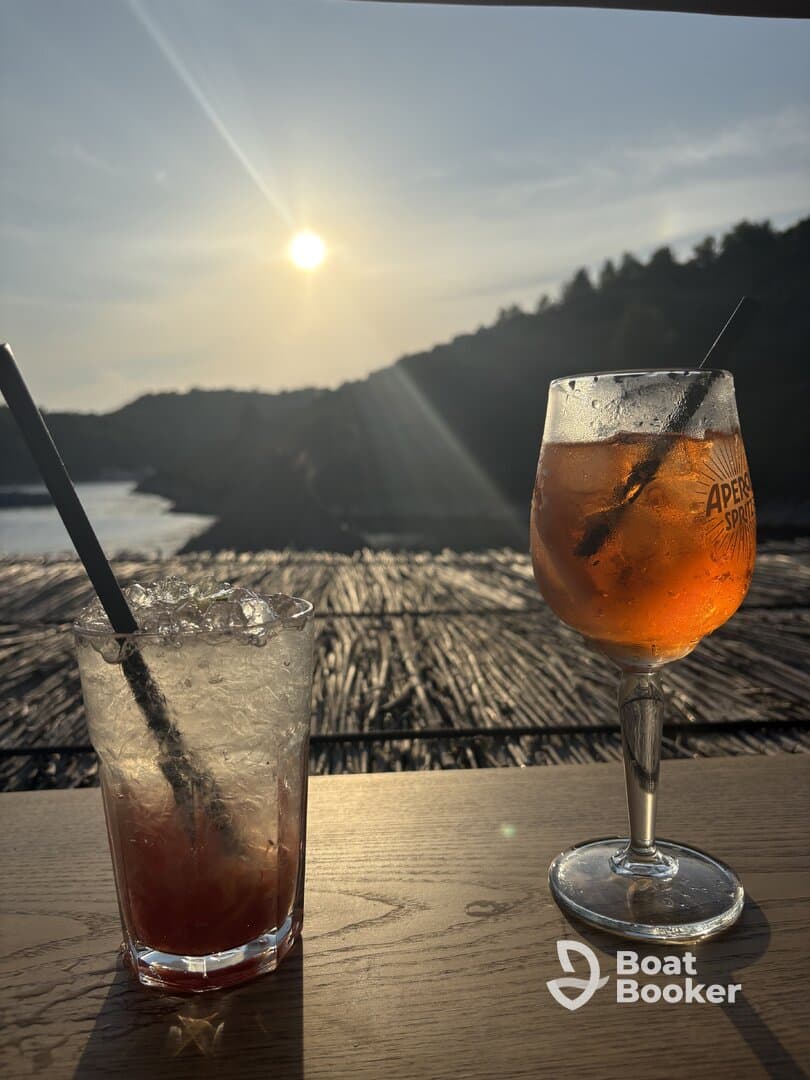 Two refreshing cocktails sit on a table, perfectly positioned to enjoy the sunset view — ideal for relaxing moments on a boat or at a seaside bar.