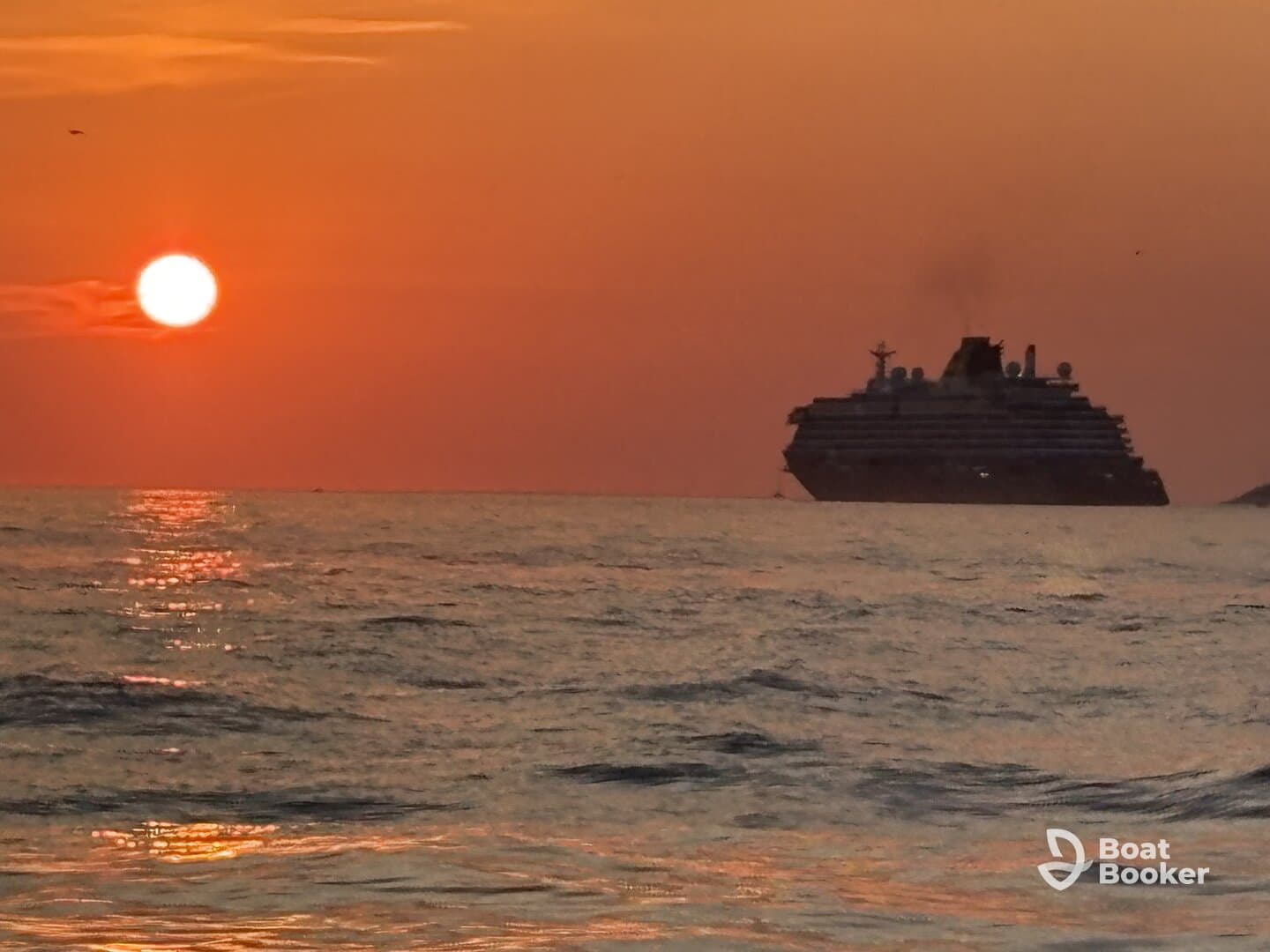 A stunning sunset casts a warm glow over a cruise ship silhouetted against the horizon, creating a picturesque maritime scene.