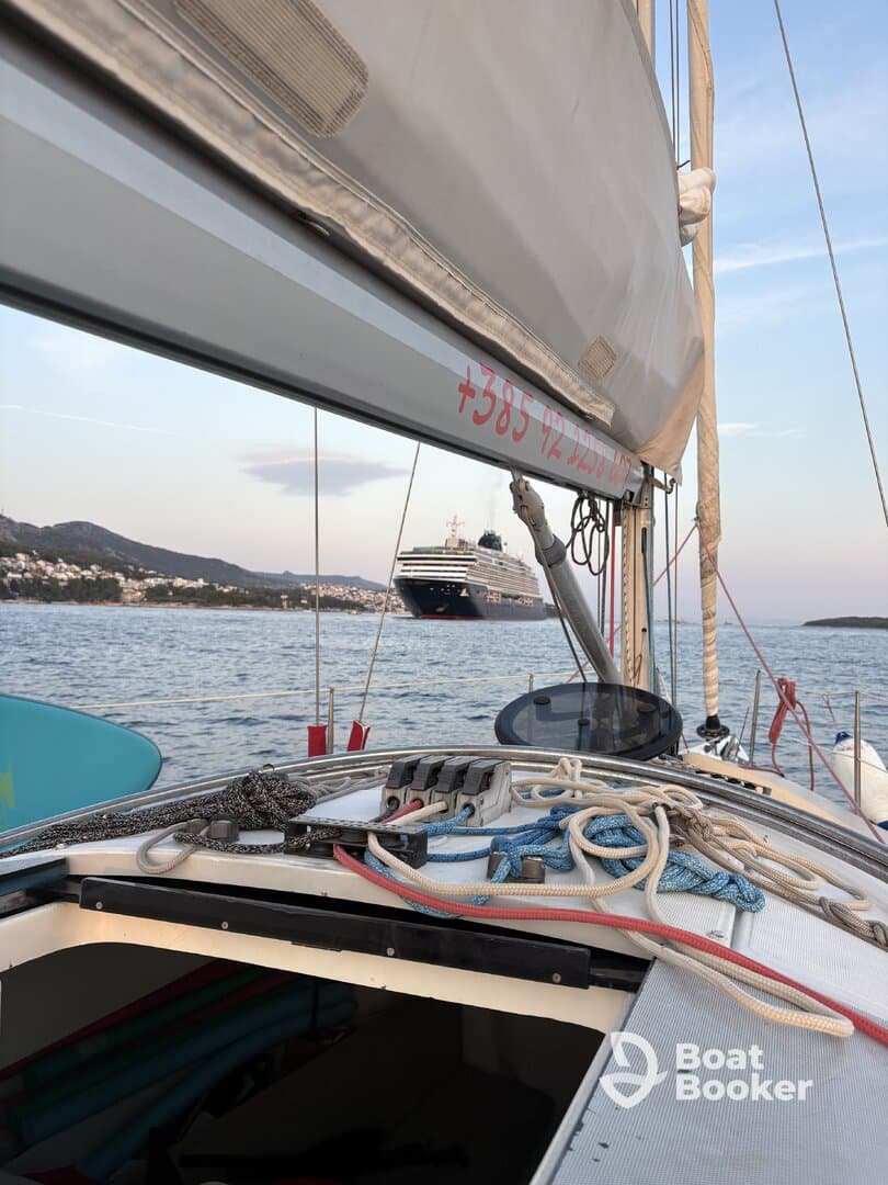 A picturesque view of a sailboat with ropes and equipment in the foreground, while a large cruise ship is anchored in the background, showcasing the beauty of sailing in coastal waters.