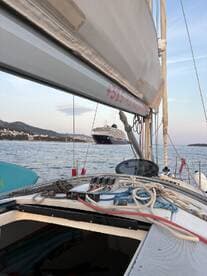 A picturesque view of a sailboat with ropes and equipment in the foreground, while a large cruise ship is anchored in the background, showcasing the beauty of sailing in coastal waters.