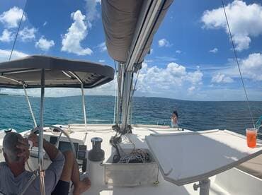 A scenic view from the helm of a sailboat, featuring a couple enjoying drinks while taking in the beautiful ocean backdrop — perfect for a relaxing day on the water.