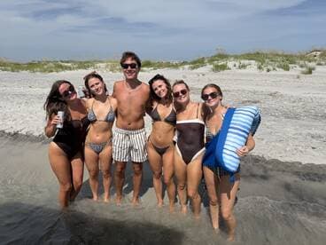 A fun group of friends enjoys a beach day, posing together in the water with drinks in hand — perfect for summer celebrations and beach parties.