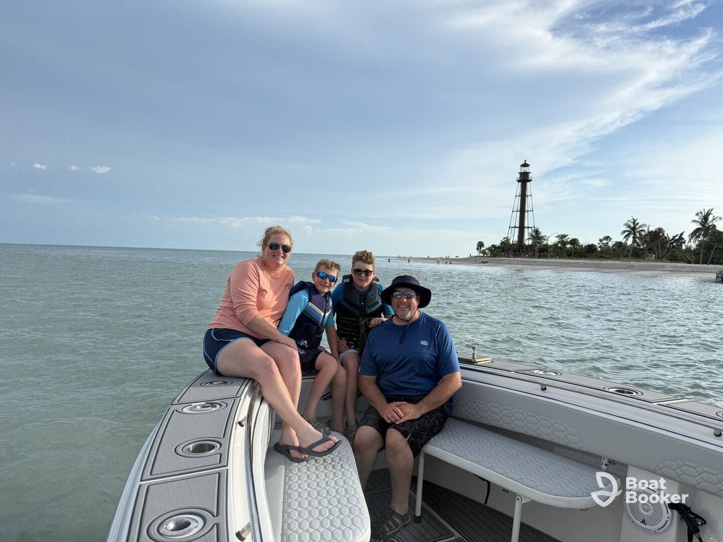 A joyful family poses on their boat with a scenic lighthouse in the background, capturing a memorable day on the water.