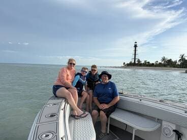 A joyful family poses on their boat with a scenic lighthouse in the background, capturing a memorable day on the water.