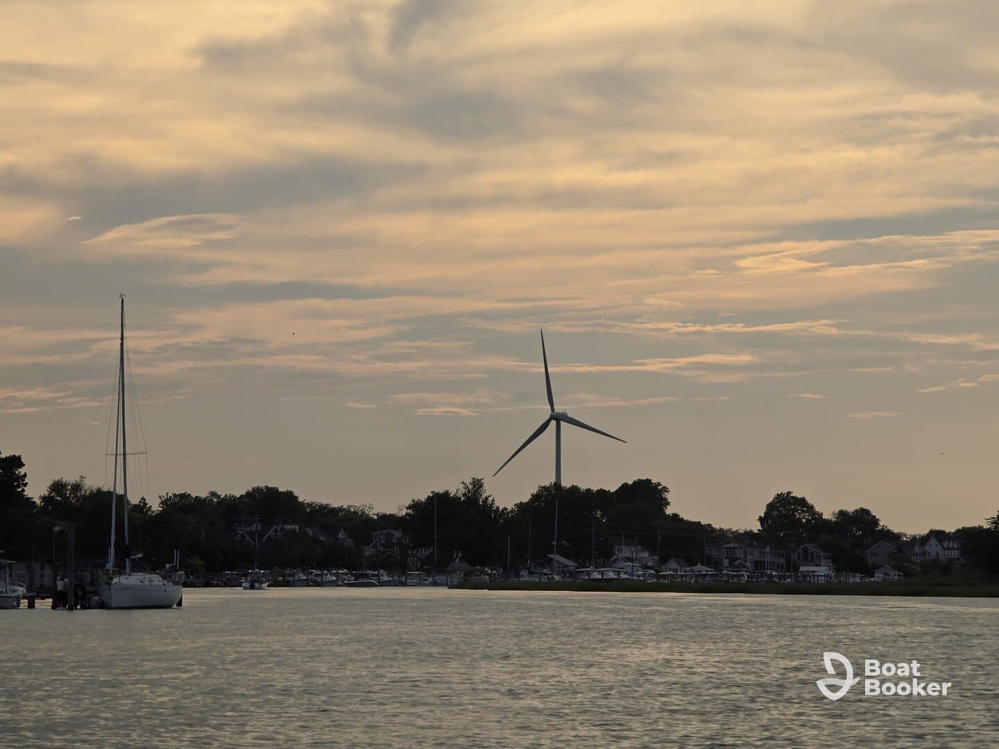 A serene sunset view featuring a sailboat and a wind turbine along the coastline, capturing the tranquil beauty of the waterfront.