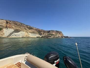 A scenic view of a rugged coastline from a boat, showcasing the clear waters and rocky cliffs — perfect for exploring nature's beauty on the water.