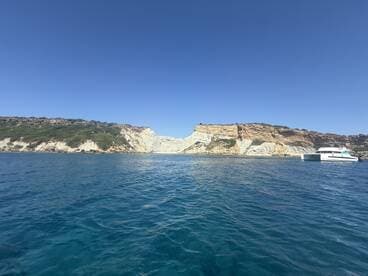 A stunning view of a catamaran anchored near a picturesque coastline, showcasing the beautiful cliffs and clear blue waters — perfect for island exploration and scenic boat trips.