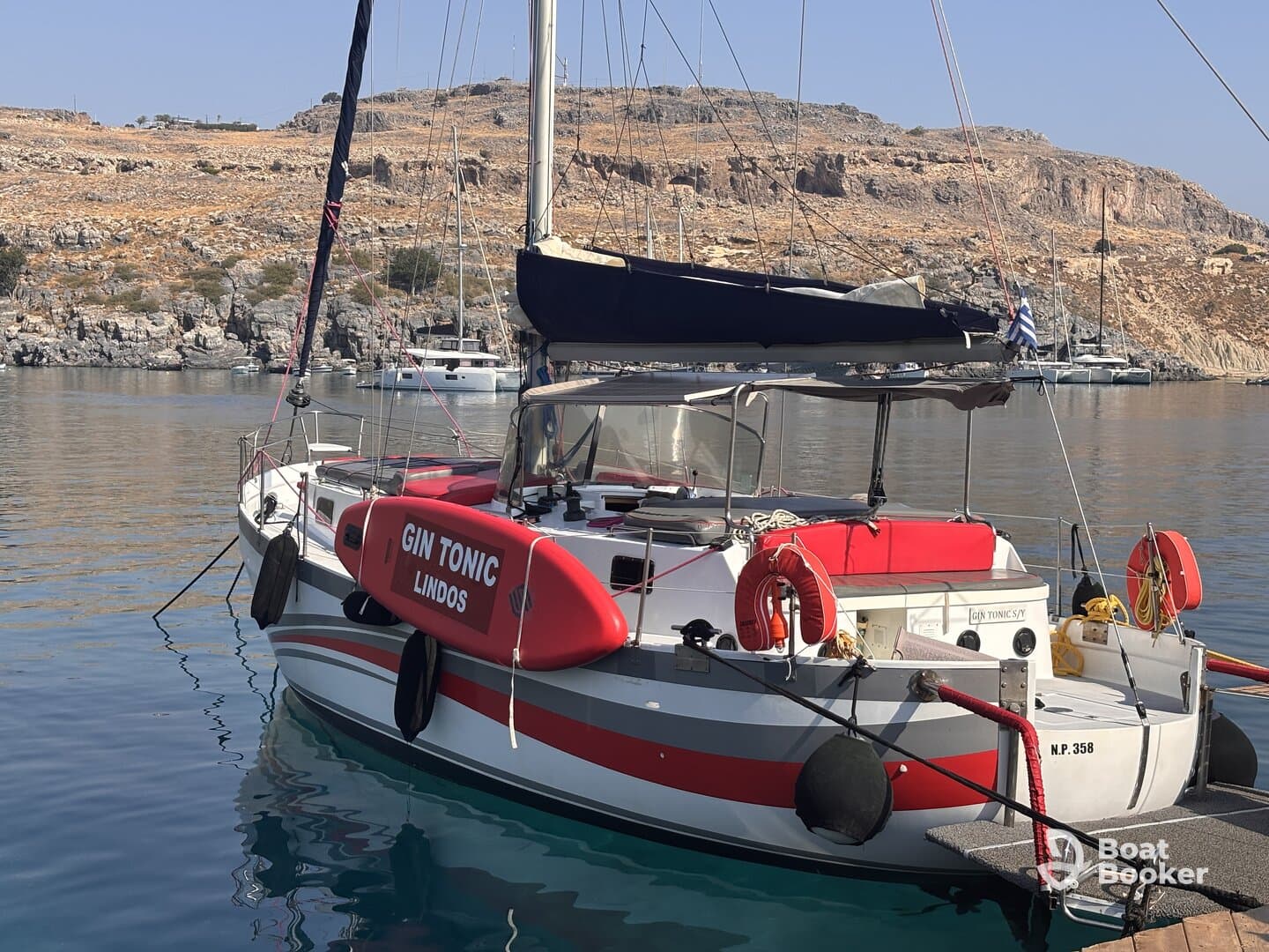 A beautifully docked yacht named 'GIN TONIC' in calm waters, showcasing its sleek design and vibrant colors against a scenic backdrop.