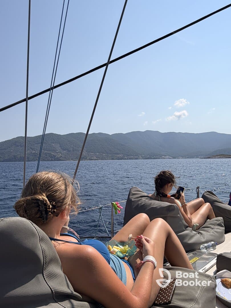 Two young women relax on a sailboat, enjoying snacks and the scenic ocean view — a perfect moment for unwinding while sailing.