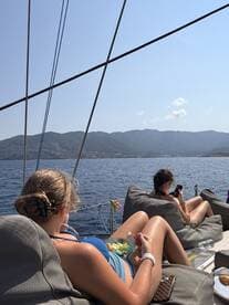 Two young women relax on a sailboat, enjoying snacks and the scenic ocean view — a perfect moment for unwinding while sailing.