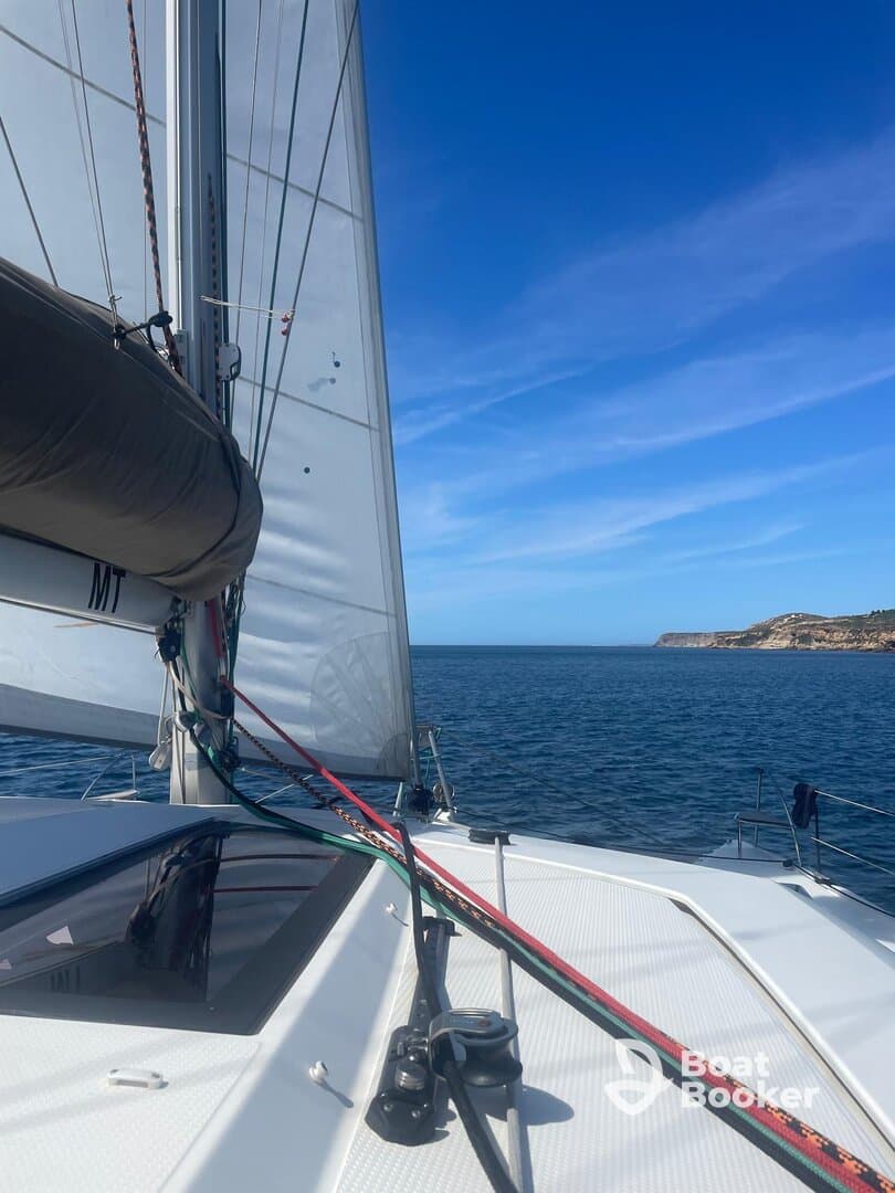 A close-up view of a sailboat's rigging and sail, showcasing the vessel's design as it navigates through calm waters under a clear blue sky.