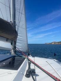 A close-up view of a sailboat's rigging and sail, showcasing the vessel's design as it navigates through calm waters under a clear blue sky.