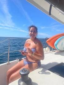 A woman enjoys a refreshing cocktail while relaxing on the deck of a yacht under a clear blue sky — perfect for summer getaways and leisurely sailing.