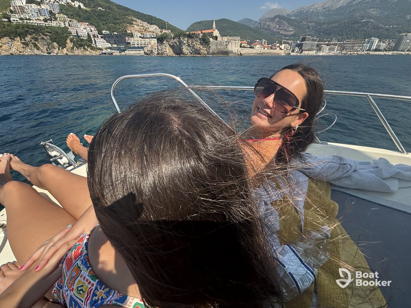 Two friends enjoy a sunny day on a boat, relaxing and soaking up the sun with a stunning coastal backdrop — perfect for a day of leisure on the water.