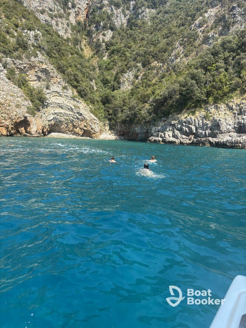 Swimmers enjoy the crystal-clear waters near a stunning rocky coastline, showcasing the beauty of outdoor adventures on the water.