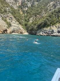 Swimmers enjoy the crystal-clear waters near a stunning rocky coastline, showcasing the beauty of outdoor adventures on the water.