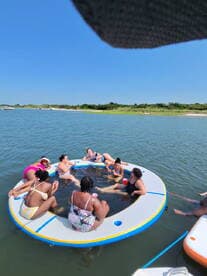 A lively group enjoys a fun day on a floating mat in the water, perfect for summer parties and relaxation with friends.