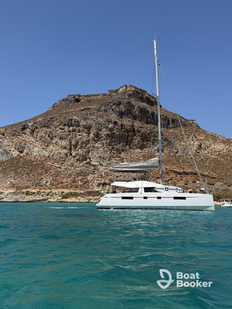 A sleek catamaran sails in clear turquoise waters, set against a stunning rocky backdrop — perfect for exploring coastal destinations.