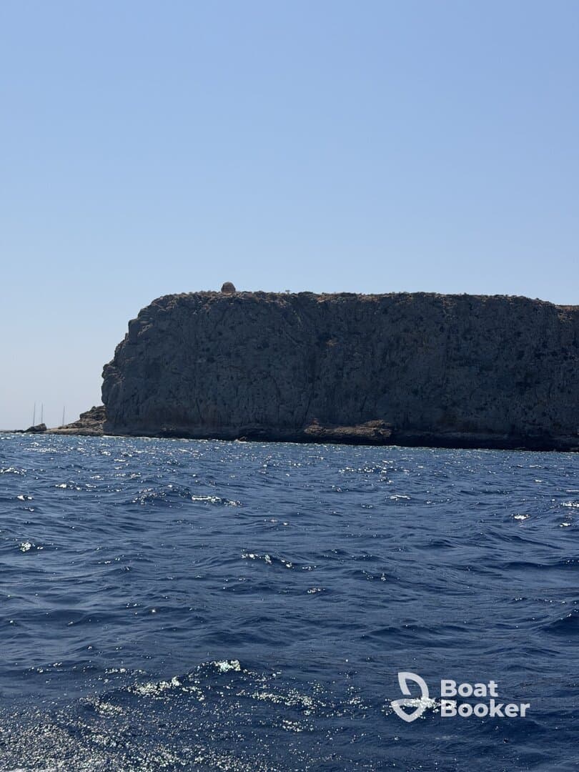An unclear view of a rocky cliff against a bright blue sky, with no identifiable features or activities.