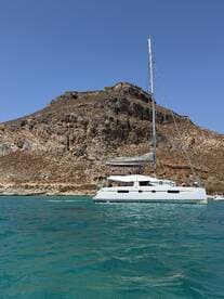 A sleek catamaran sails in clear turquoise waters, set against a stunning rocky backdrop — perfect for exploring coastal destinations.