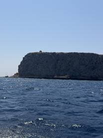 An unclear view of a rocky cliff against a bright blue sky, with no identifiable features or activities.