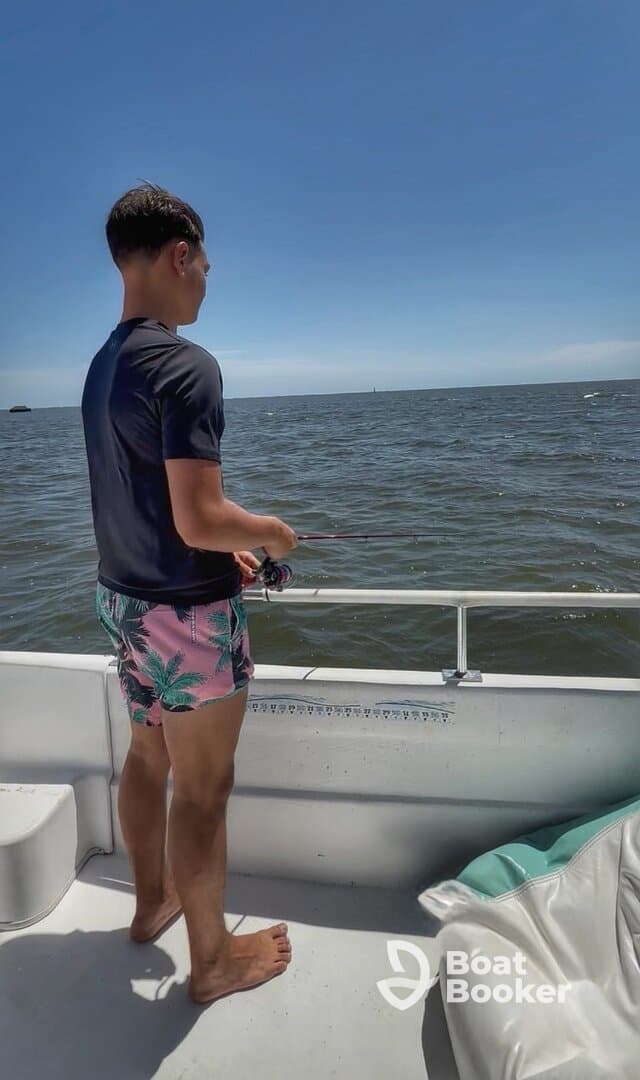 A young adult enjoys a day of fishing on a boat, casting a line into the open ocean under a clear blue sky.