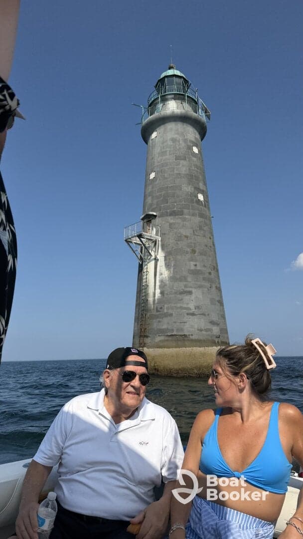 A couple enjoys a scenic boat ride near a historic lighthouse, capturing a moment of connection against a beautiful ocean backdrop.