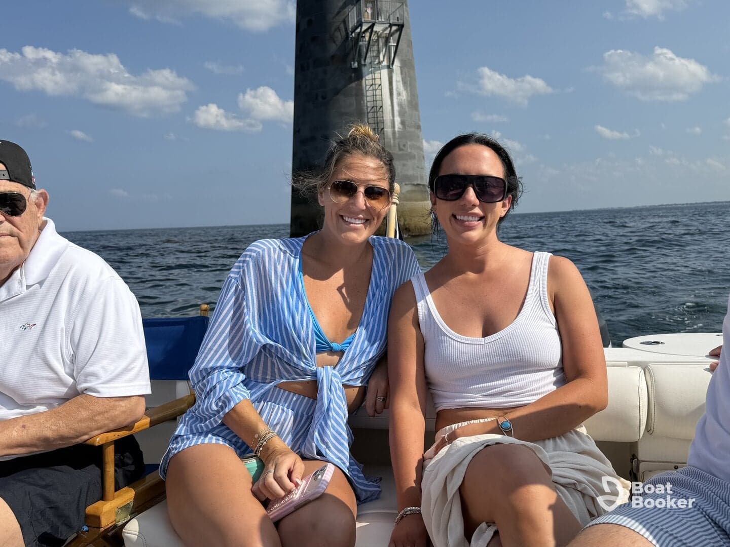 Two friends enjoy a sunny day on the water, posing for a photo with a lighthouse in the background — a perfect moment for boating adventures.