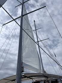 A close-up view of the mast and sail of a sailboat against a cloudy sky, showcasing the intricate rigging and design typical of sailing vessels.