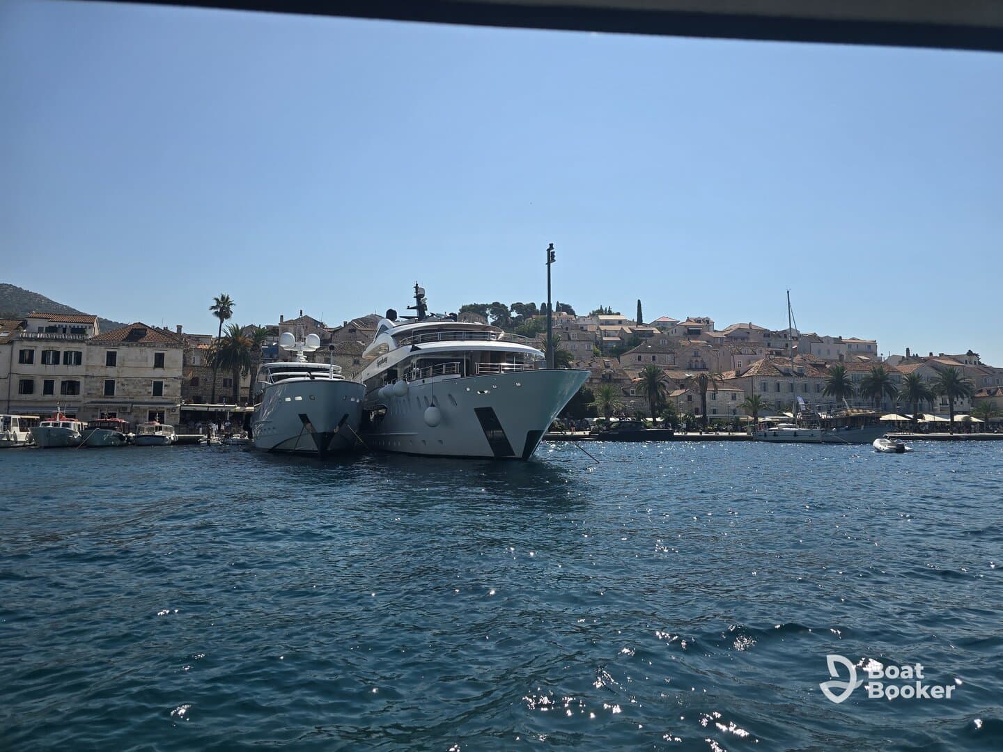 A stunning view of two luxurious yachts docked in a picturesque harbor, showcasing the charm of coastal architecture and clear blue waters.