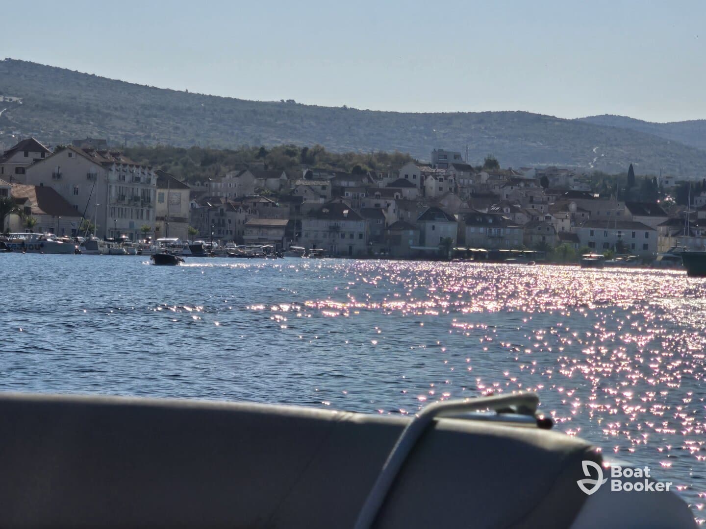 A picturesque view of a harbor with charming buildings along the coastline, reflecting sunlight on the water — a perfect backdrop for a boating adventure.