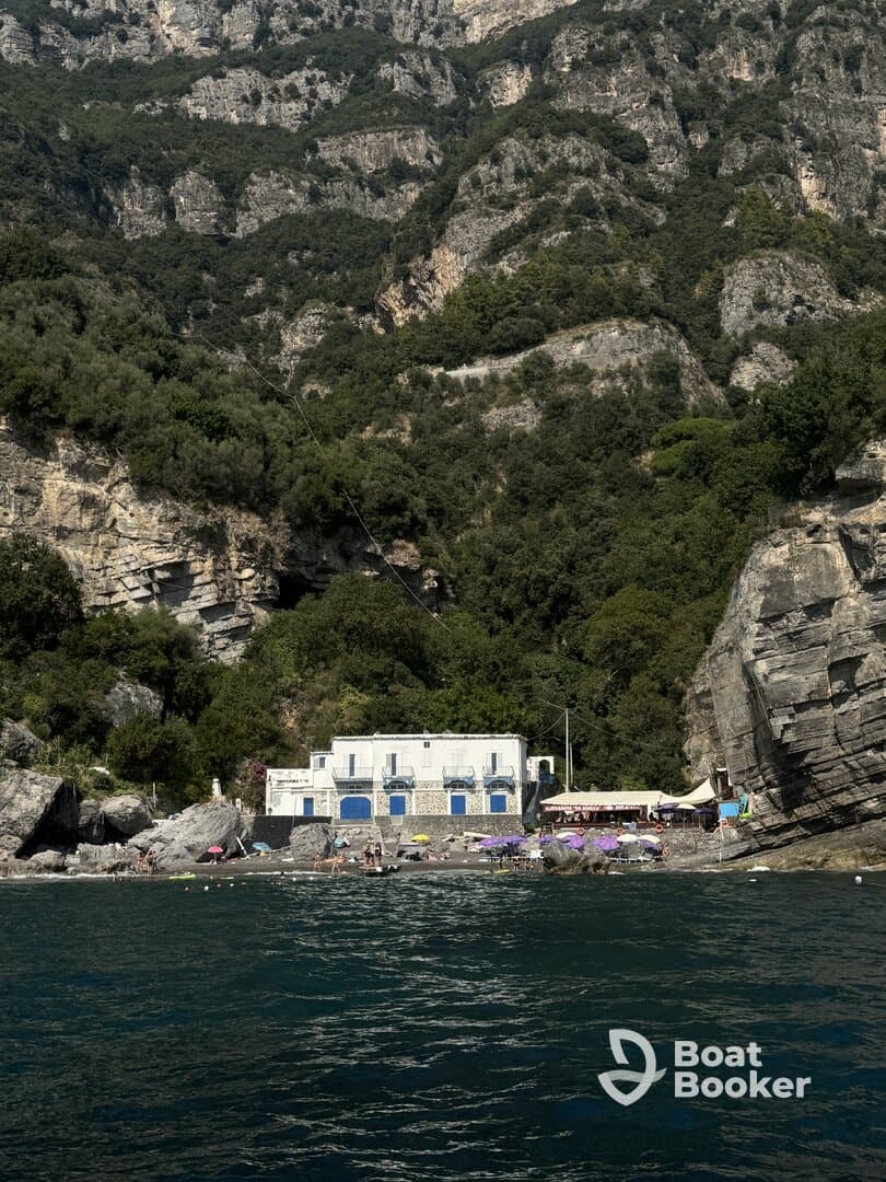 A scenic view of a beach with a charming building and guests enjoying the sun, surrounded by stunning cliffs — a perfect destination for relaxation and exploration.