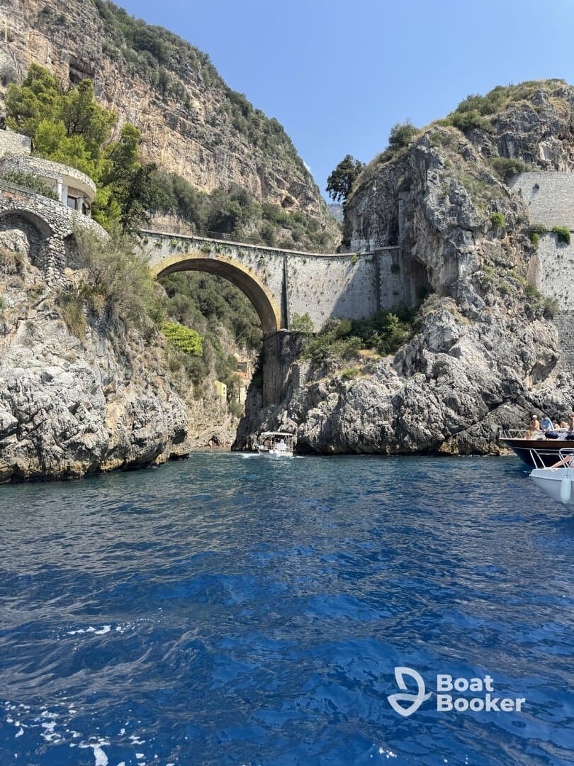 A stunning view of a coastal bridge surrounded by rocky cliffs, with boats navigating the crystal-clear waters — a perfect representation of the beautiful scenery along the coastline.