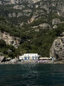 A scenic view of a beach with a charming building and guests enjoying the sun, surrounded by stunning cliffs — a perfect destination for relaxation and exploration.