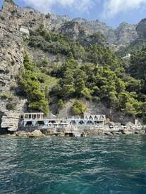 A stunning view of a coastal restaurant nestled among rocky cliffs, showcasing the beautiful scenery of the Amalfi Coast — perfect for dining with a picturesque backdrop.