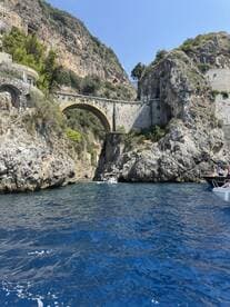 A stunning view of a coastal bridge surrounded by rocky cliffs, with boats navigating the crystal-clear waters — a perfect representation of the beautiful scenery along the coastline.