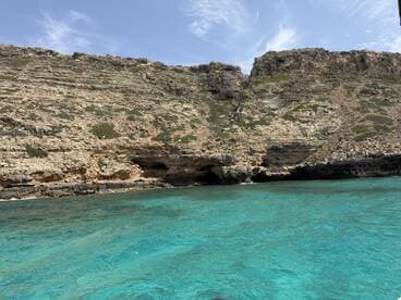 A stunning view of rocky cliffs meeting crystal-clear turquoise waters, showcasing the natural beauty of the coastline — perfect for exploring by boat.