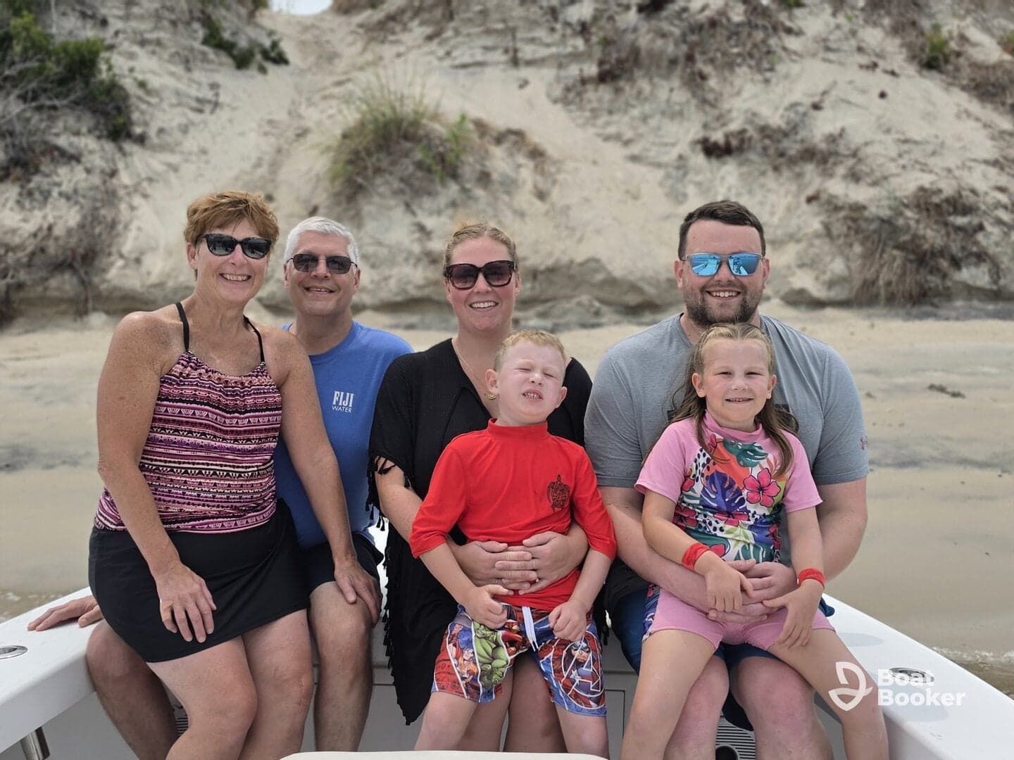 A cheerful family poses together on a boat with a sandy beach backdrop, capturing a memorable moment during their boating adventure.