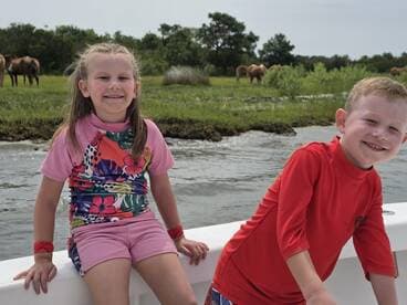 Two children enjoy a fun day on the boat, smiling as they take in the scenic view of wild horses grazing nearby — a perfect family adventure on the water.