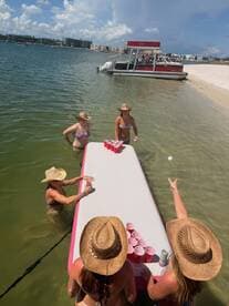 A lively group enjoys a fun beach day playing beer pong in the water, with a pontoon boat anchored nearby — perfect for summer celebrations and group activities.