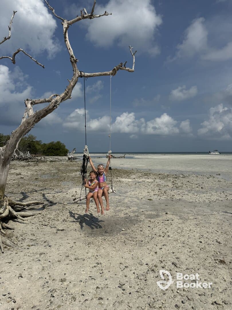 Two children enjoy swinging from a tree on a sandy beach, capturing the essence of fun and adventure in a tropical setting.
