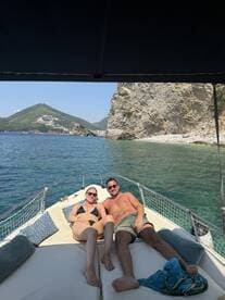 A couple relaxes on the bow of a boat, enjoying the sun and stunning coastal scenery — a perfect moment for a romantic getaway on the water.