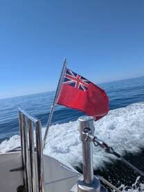 A close-up view of a boat's flag waving in the wind as it moves through calm waters, showcasing the vessel's journey on a clear day.