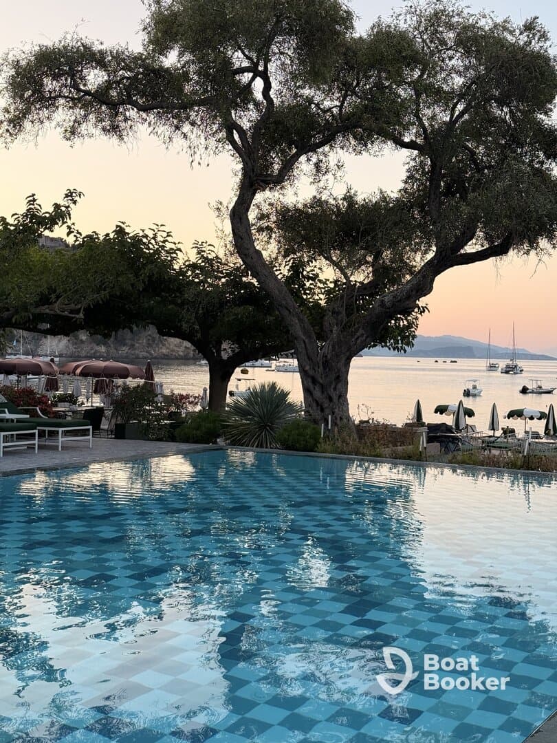 A tranquil scene featuring a pool reflecting the surrounding trees and distant boats, creating a serene atmosphere perfect for relaxation.
