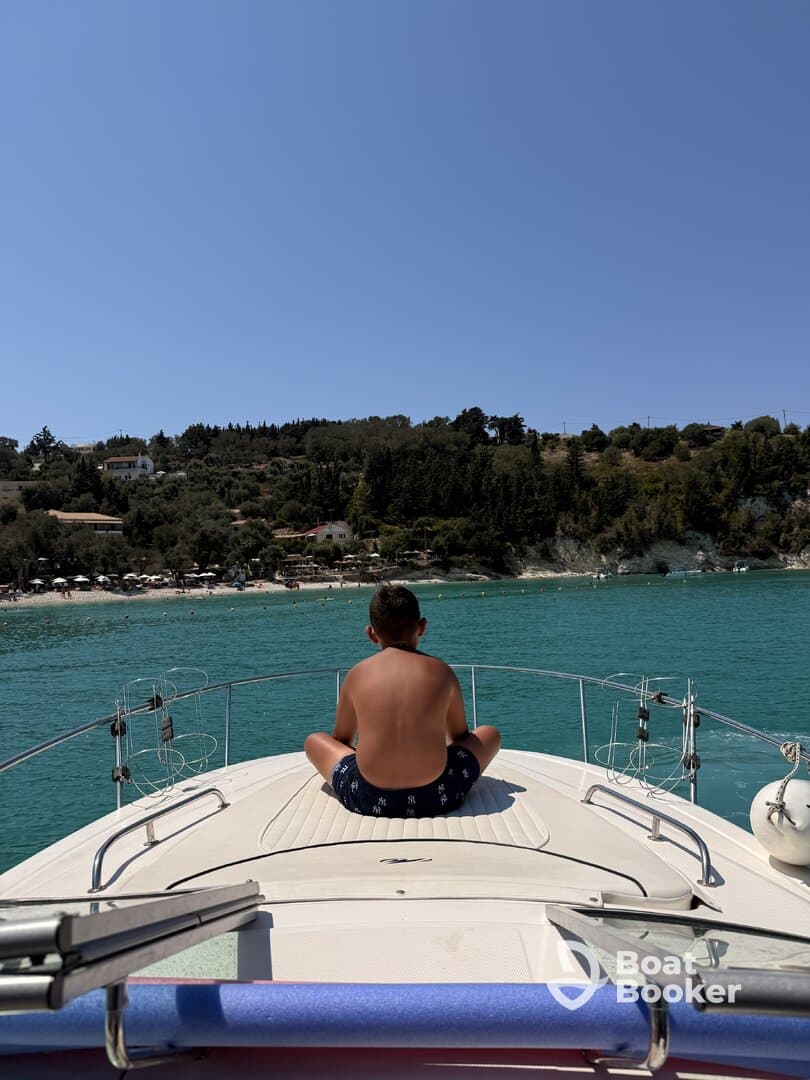 A young boy enjoys a serene moment on the bow of a boat, overlooking a beautiful beach and turquoise waters — a perfect summer getaway.