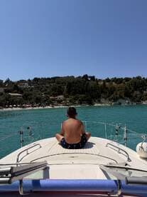 A young boy enjoys a serene moment on the bow of a boat, overlooking a beautiful beach and turquoise waters — a perfect summer getaway.