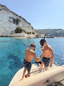 Two children prepare to snorkel off the side of a boat, surrounded by stunning turquoise waters and dramatic cliffs — a perfect adventure for young explorers.