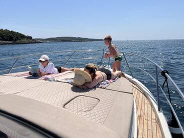 A family enjoys a sunny day on the boat, with one child playing and another reading, capturing the essence of summer relaxation on the water.